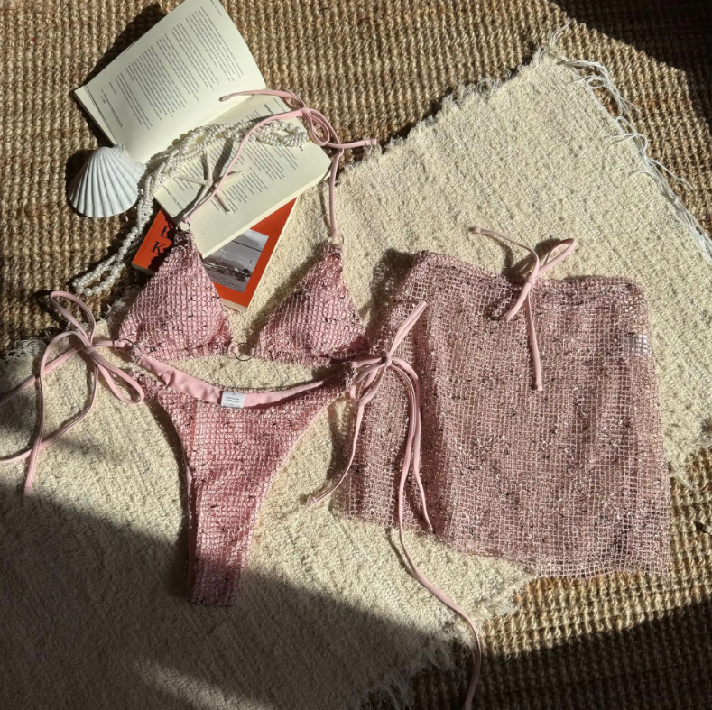 Flat lay of Aurora pink textured bikini and matching sheer mini skirt set with triangle top and tie-side bottoms.