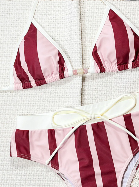 Close-up of pink and burgundy striped bikini with white contrast binding, bead detail and adjustable waist tie.