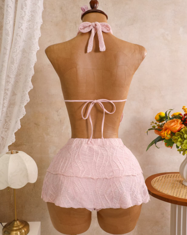 Back view of blush textured bikini and tiered mini skirt set with halter neck tie, back tie and soft flared skirt.