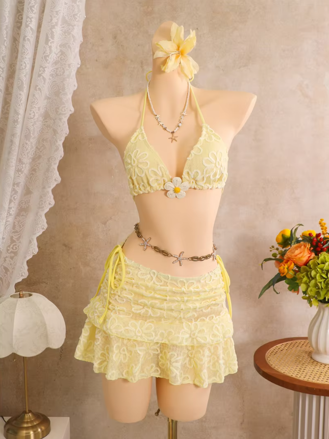 Daffodil floral embroidered bikini and sheer tiered mini skirt set displayed on mannequin with halter ties and flower appliqué.