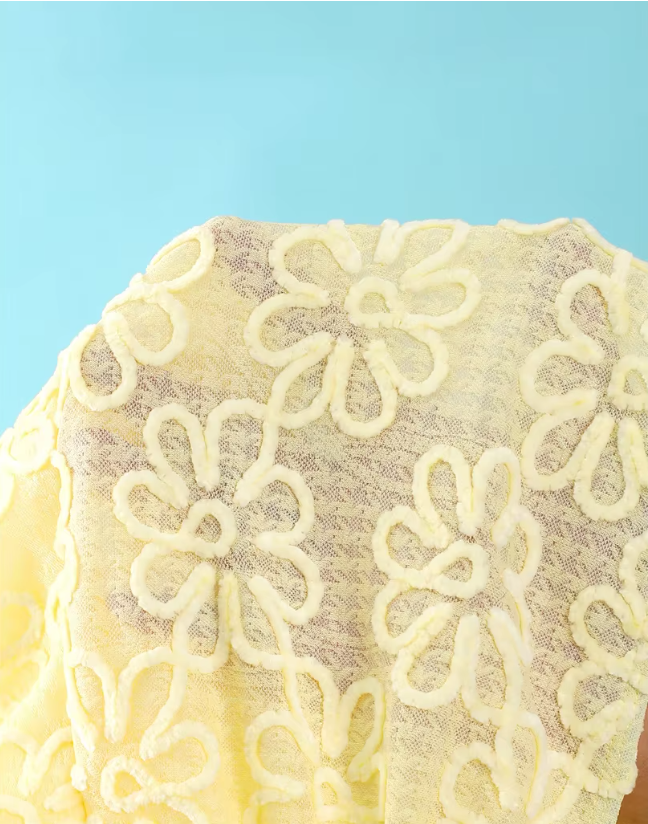 Close-up of daffodil sheer floral embroidered fabric with raised flower texture and soft mesh-look finish.