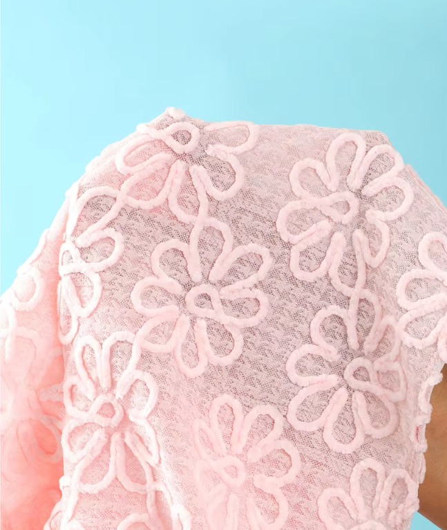 Close-up of pink sheer floral embroidered fabric with raised flower texture and soft mesh-look finish.