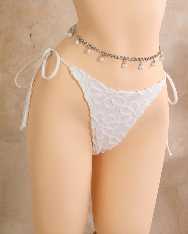 Close-up of white floral embroidered bikini bottoms with side-tie fastening and raised flower texture.