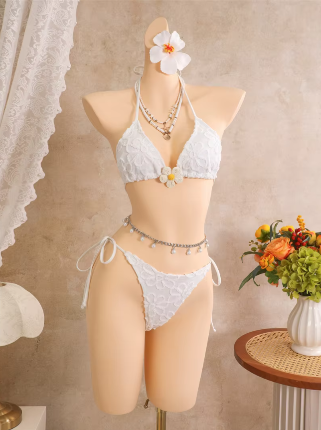 White floral embroidered triangle bikini set with flower centre accent and tie-side high-leg bottoms on mannequin.