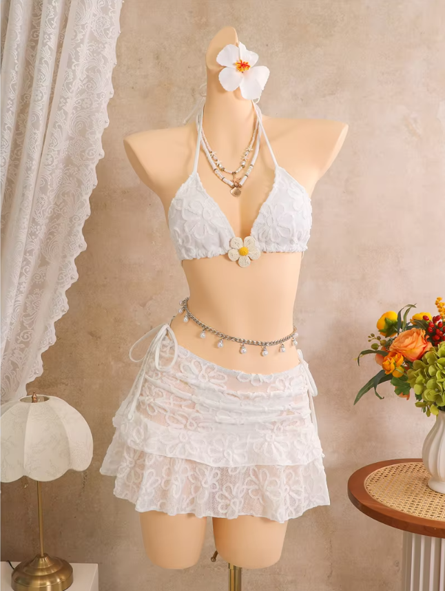 White floral embroidered bikini and sheer tiered mini skirt set displayed on mannequin with halter ties and flower appliqué.