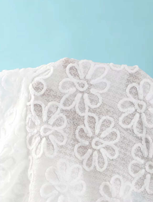 Close-up of white sheer floral embroidered fabric with raised flower texture and soft mesh-look finish.