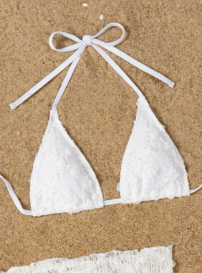 Close-up of white Cabana lace triangle bikini top with halter ties and floral appliqué texture on sand.