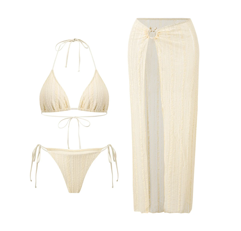 Flat lay of the Cabo Bikini & Skirt Set in ivory, including a halter triangle bikini top, tie-side bikini bottoms and a matching textured maxi skirt with a front split.