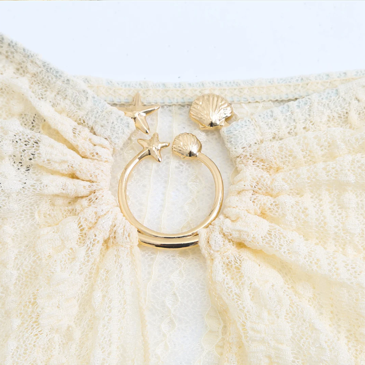 Close-up detail of the Cabo Bikini & Skirt Set in ivory, highlighting the gold ring hardware with shell and starfish charm accents.