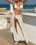 Model standing on the beach wearing the Cabo Bikini & Skirt Set in ivory, featuring a halter triangle bikini top, tie-side bikini bottoms and a sheer textured maxi skirt with a high front split.