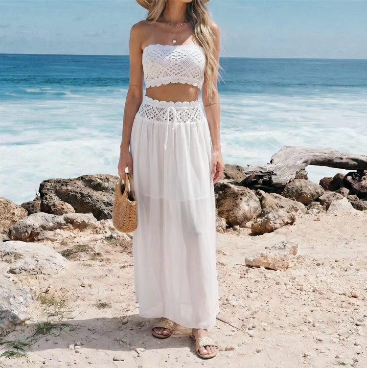 Full front view of white crochet-look crop top and sheer maxi skirt resort set worn by model by the ocean.