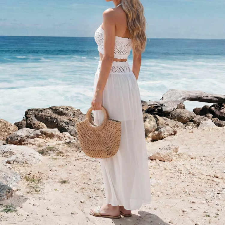 Back side view of white crochet-look crop top and flowing sheer maxi skirt set worn by model seaside.