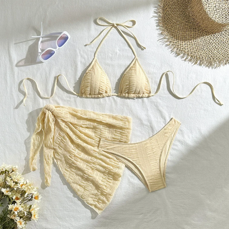 Ivory textured bikini and matching tie sarong set arranged in a beach flat lay with resort accessories.