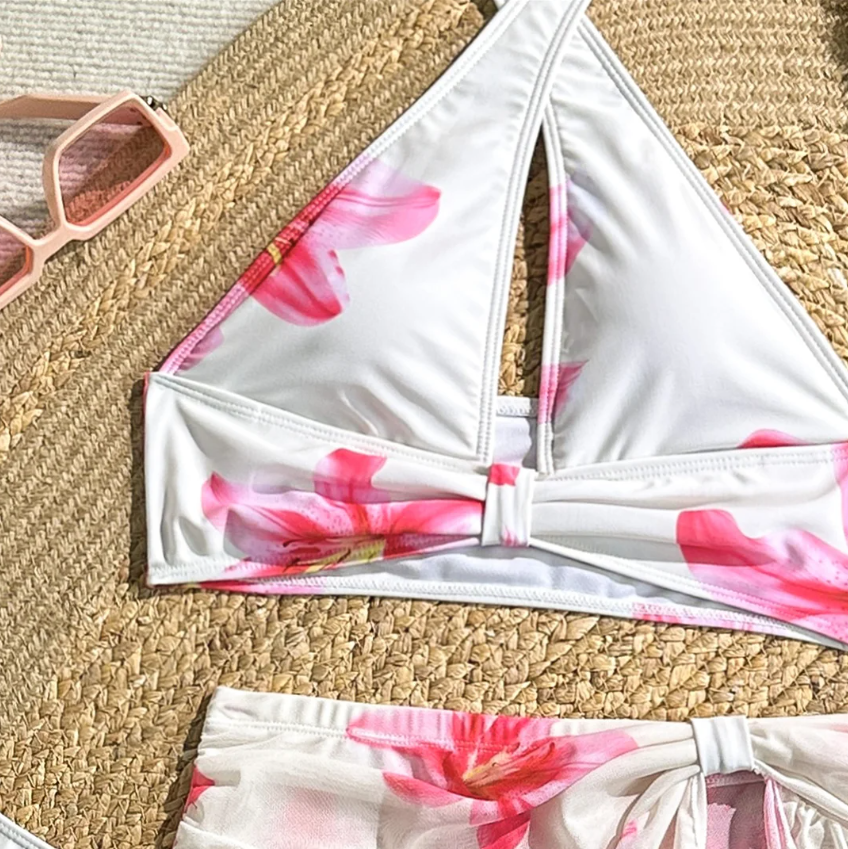 Close-up of Camellia white floral halter bikini top and matching skirt set with pink lily print and twist-front detail.