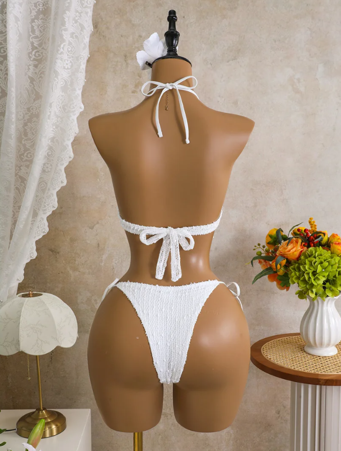 Back view of white textured bikini set on mannequin with halter neck tie, back tie and high-leg bikini bottoms.