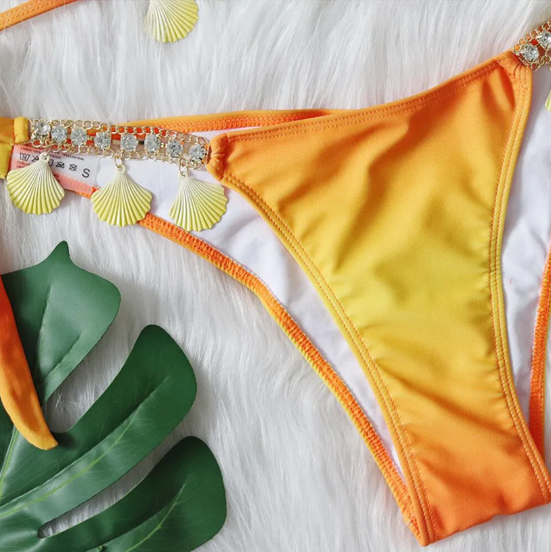 Close-up of Cancún orange bikini bottoms with rhinestone side detail, shell charms and smooth lined finish.