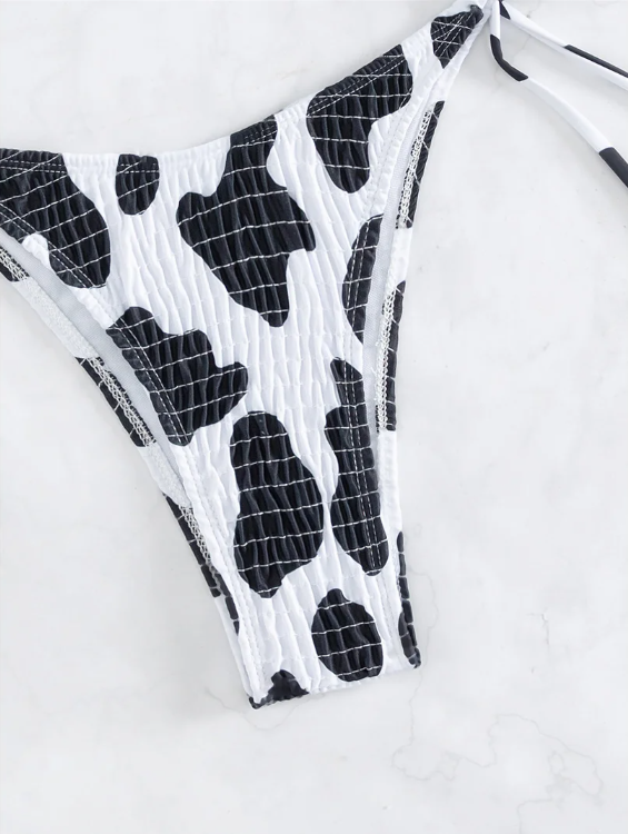 Close-up of black and white cow print bikini bottoms with crinkle texture and tie-side fastening.