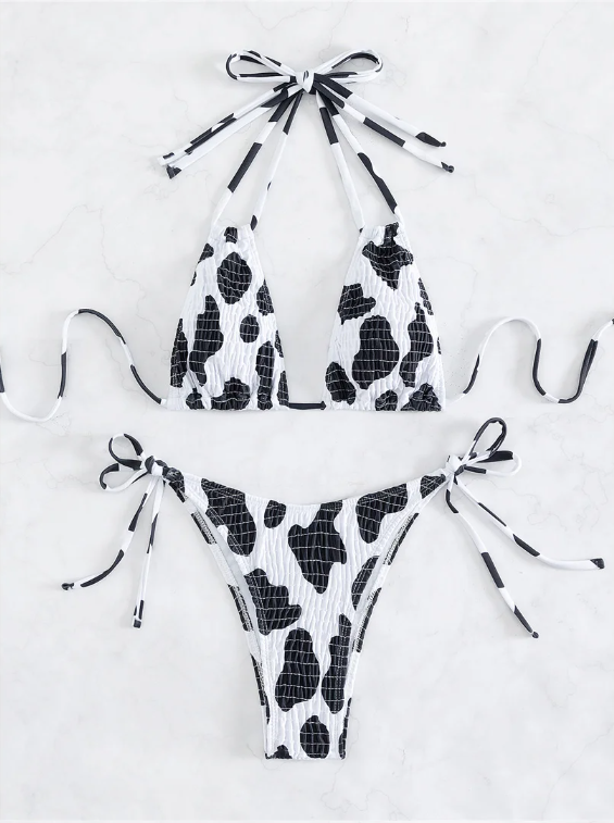 Black and white cow print triangle bikini set with crinkle texture and tie-side bottoms in a flat lay.