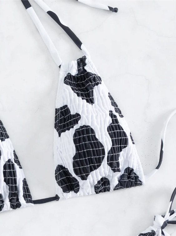 Close-up of black and white cow print triangle bikini top with crinkle texture and adjustable ties.