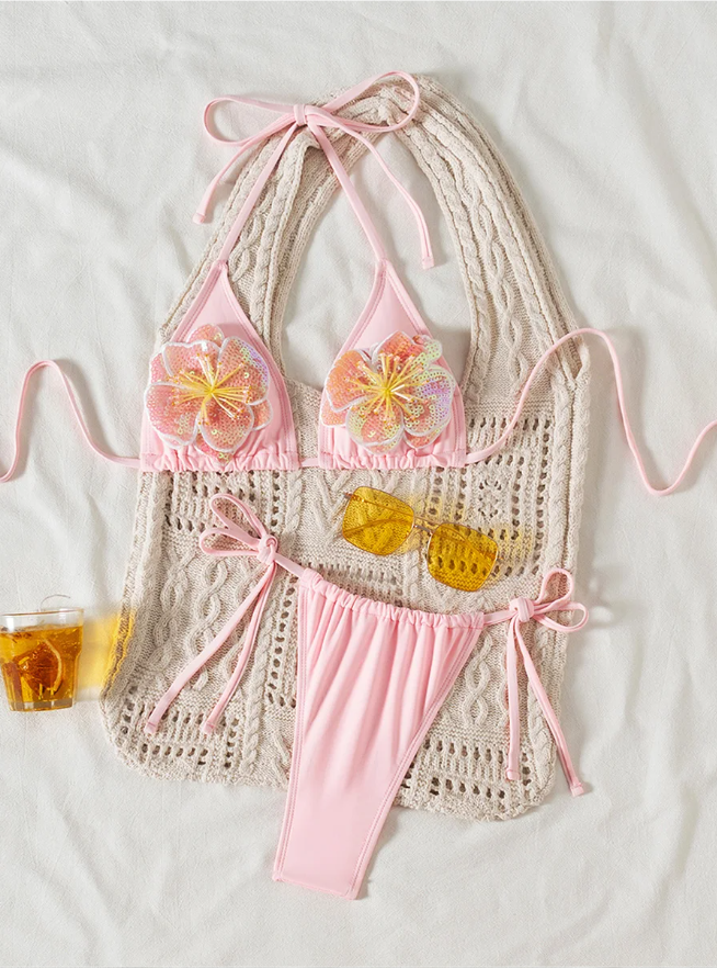 Flat lay of Coral Bay pink bikini set with triangle halter top, floral sequin appliqué and tie-side bottoms.