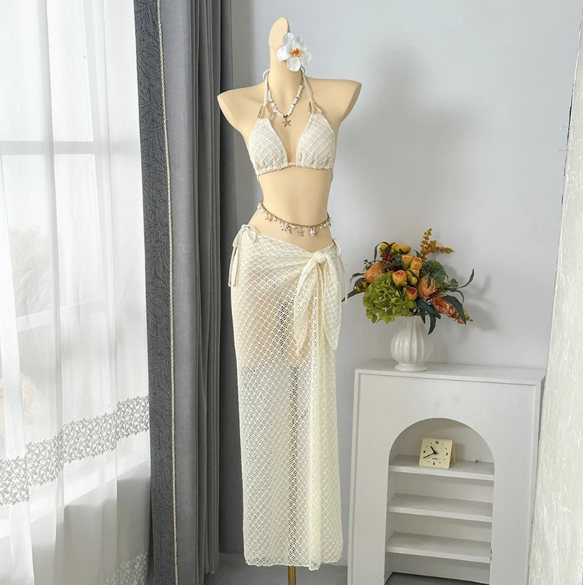 Ivory openwork halter bikini and matching maxi sarong set displayed on mannequin with resort styling.
