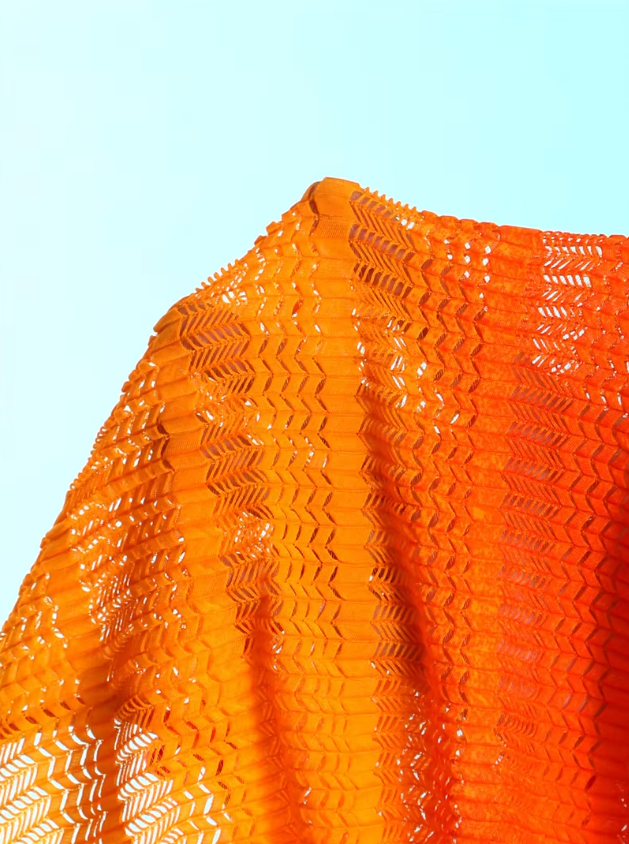 Close-up of the Saffron Estelle openwork fabric with orange gradient texture and sheer crochet-look finish.