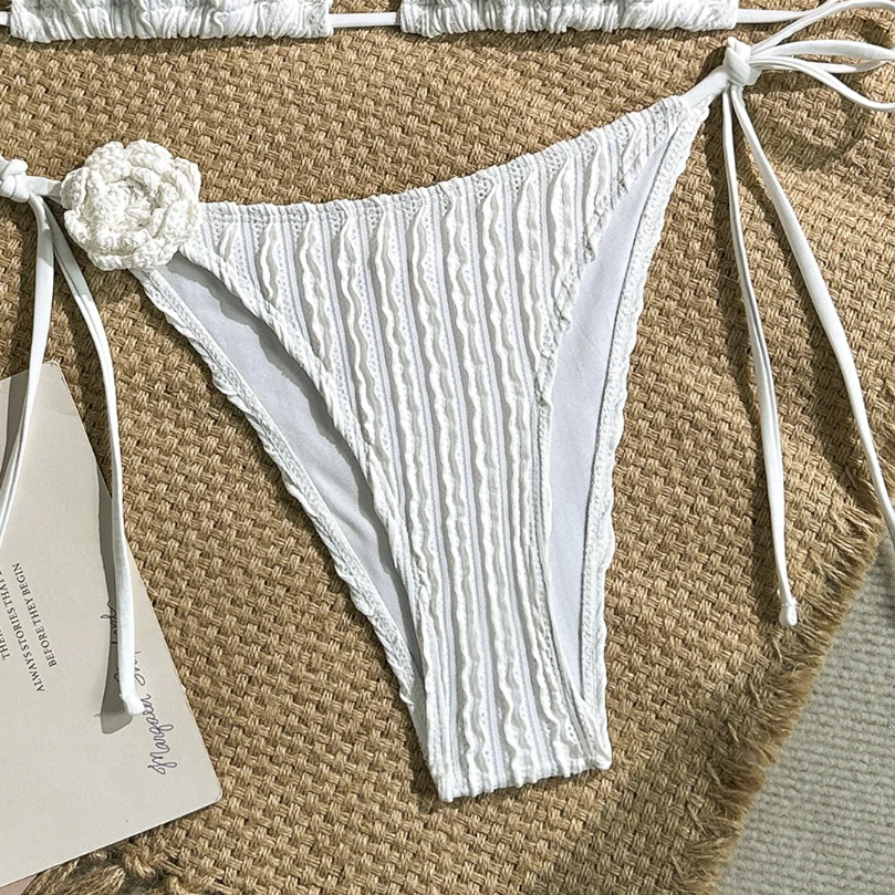 Close-up of white textured bikini bottoms with high-leg cut, tie-side fastening and floral appliqué detail.