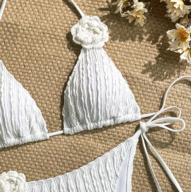 Close-up of white textured triangle bikini top with ribbed surface detail and floral appliqué accent.