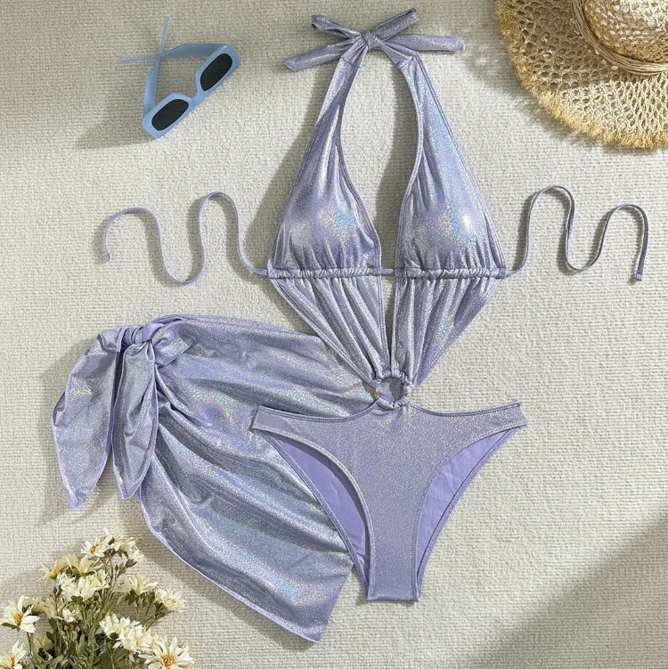 Flat lay of the Èze Iridescent Sarong Set in shimmering lilac, featuring a cut-out halter one-piece and matching tie sarong.
