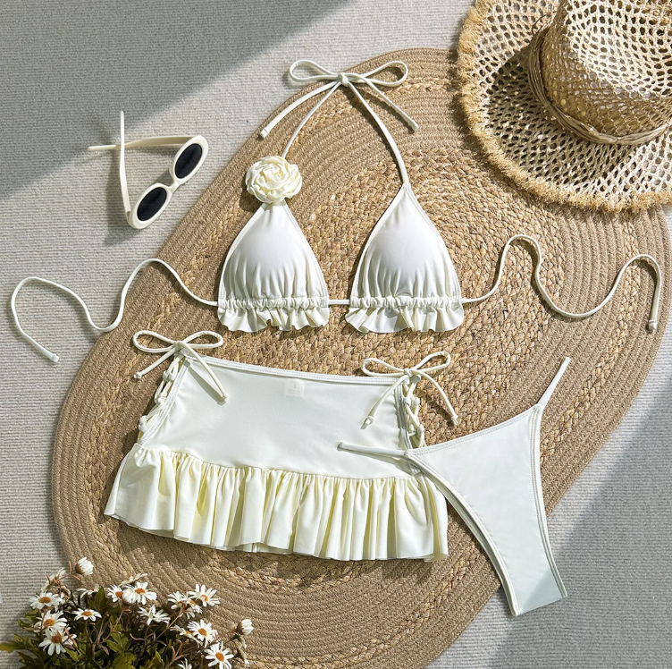 White bikini and matching mini skirt set flat lay with rosette halter top and frill-trim skirt.