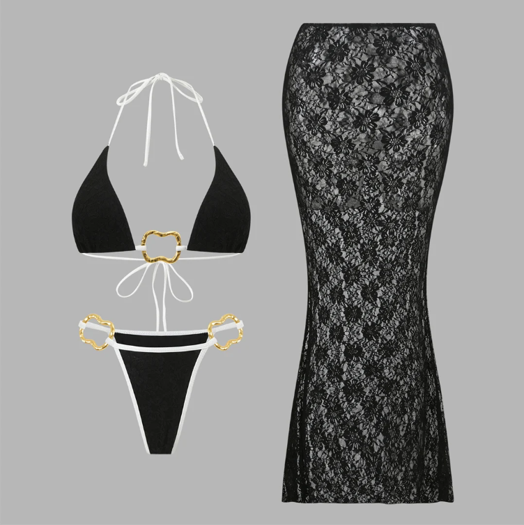 Flat lay of the Grenada Bikini & Skirt Set in black, including a triangle bikini top, matching bikini bottoms with gold hardware and a coordinating sheer floral lace maxi skirt.