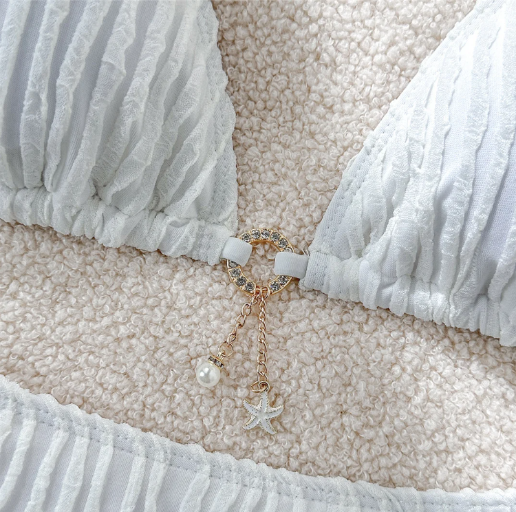 Close-up of the Isla Bikini Set centre detail, featuring a gold ring connector with pearl and starfish charms on white textured fabric.