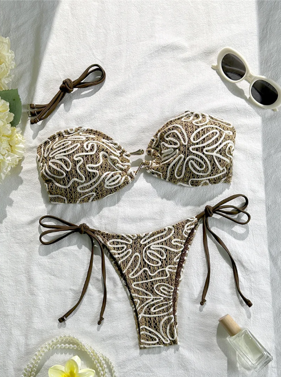 Brown crochet-look bandeau bikini set with cream cord embroidery, gold-tone hardware and tie-side bottoms in a flat lay.