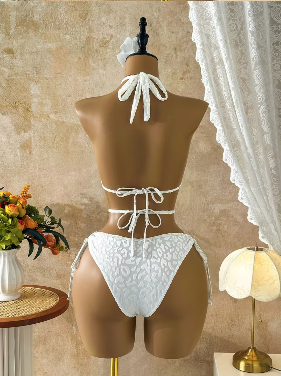 Back view of white tonal leopard one-piece swimsuit with halter tie, back tie fastening and high-leg tie-side bottoms.