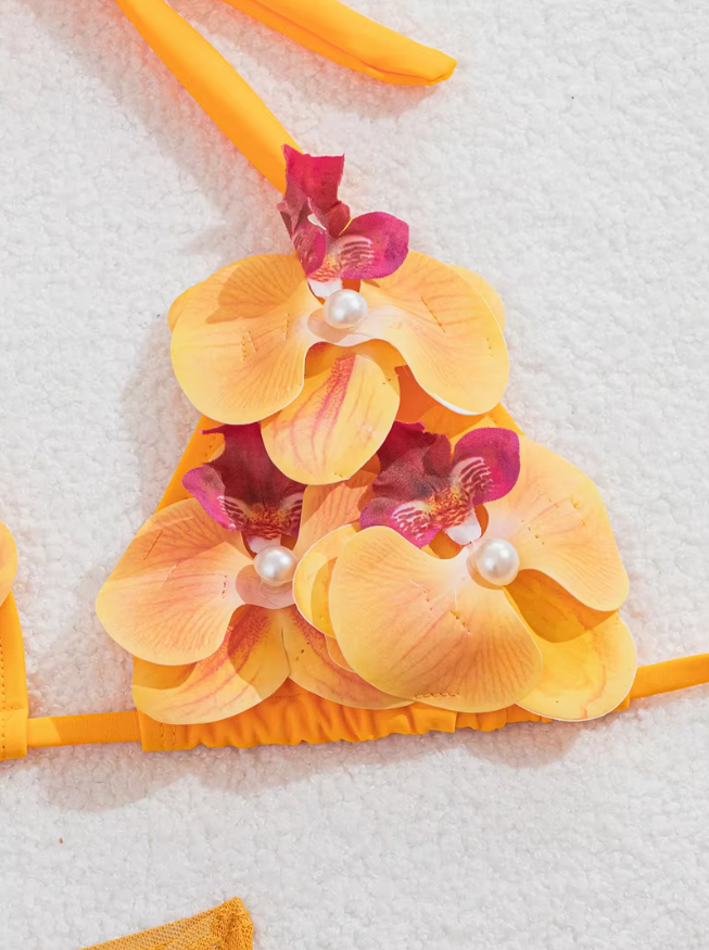 Close-up of orange bikini top with dimensional orchid appliqué and pearl-look floral centre accents.