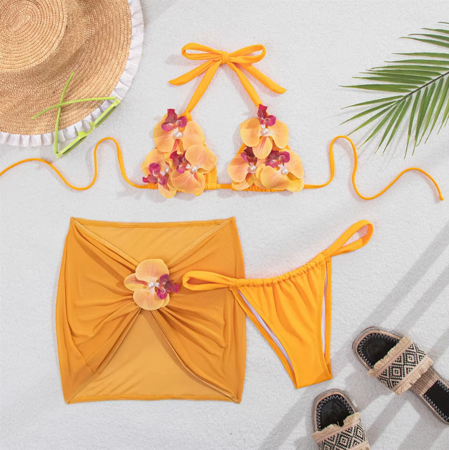 Kalani orange bikini and skirt set flat lay with orchid appliqué triangle top, tie-side bottoms and sheer mini skirt.