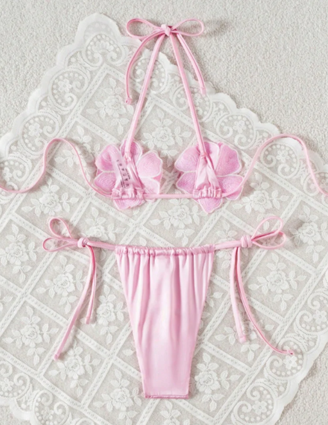 Back flat lay of pink string bikini set showing halter ties, flower appliqué backs and gathered tie-side bottoms.