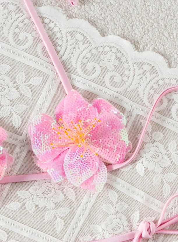 Close-up of pink sequin flower appliqué on bikini top with yellow centre detailing and slim halter strap.