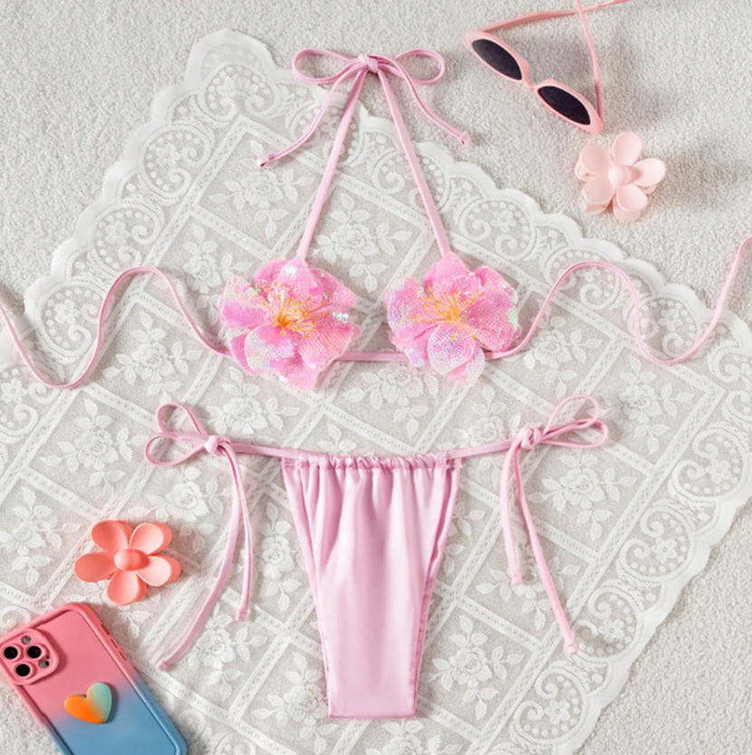 Lanai pink bikini set flat lay with oversized sequin flower appliqué top and gathered tie-side bottoms.