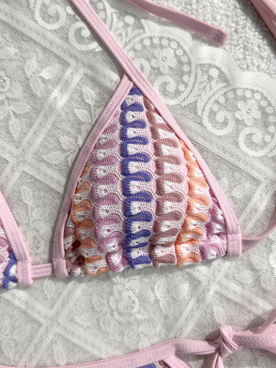 Close-up of pastel crochet-look triangle bikini top with pink binding and adjustable halter ties.