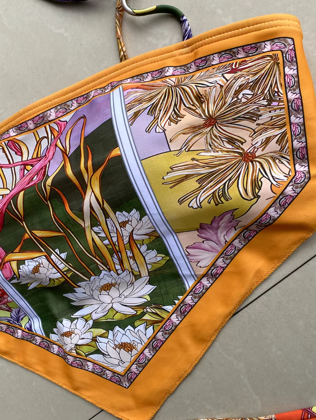 Close-up of Madeira bandeau bikini top with orange border, floral botanical scarf print and smooth swim fabric.