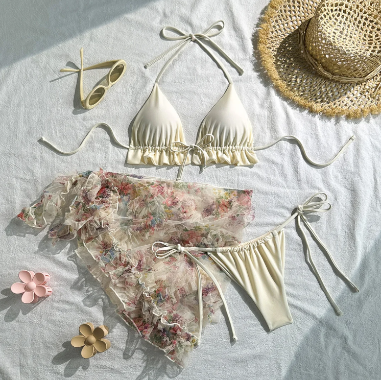 Malibu bikini and sarong set laid flat featuring an ivory frill triangle bikini and a sheer floral ruffle sarong.