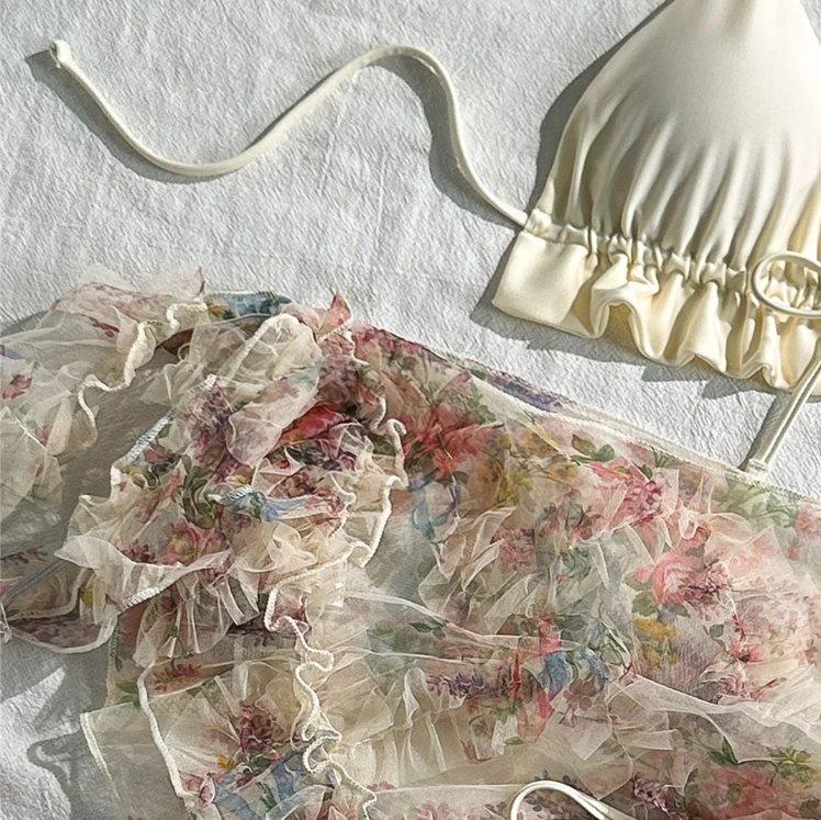 Close-up of the Malibu set showing the ivory bikini top and sheer floral sarong with layered ruffle trim.