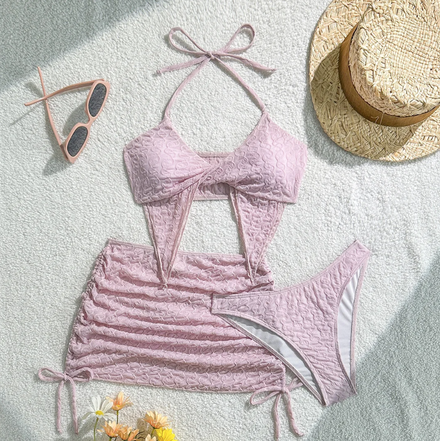 Flat lay of Maya pink textured bikini and mini skirt set with twist-front halter top, ruched skirt and high-leg bottoms.