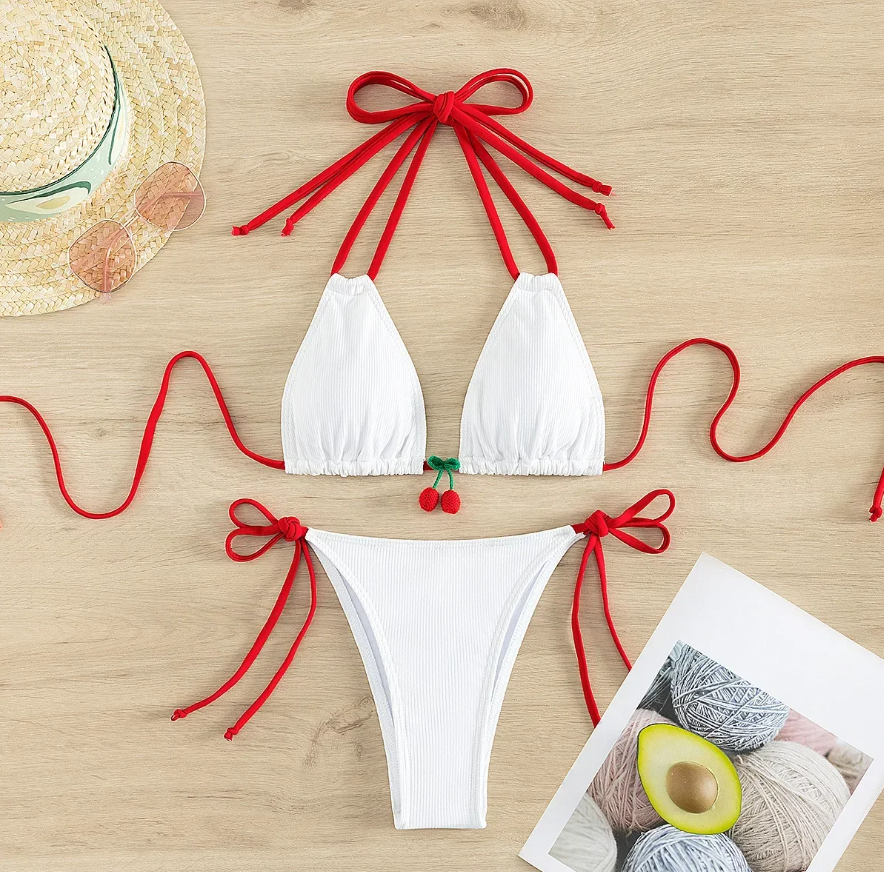 Flat lay view of white ribbed bikini set with contrast red halter and side ties, featuring a triangle bikini top and matching bottoms with a cherry charm detail.