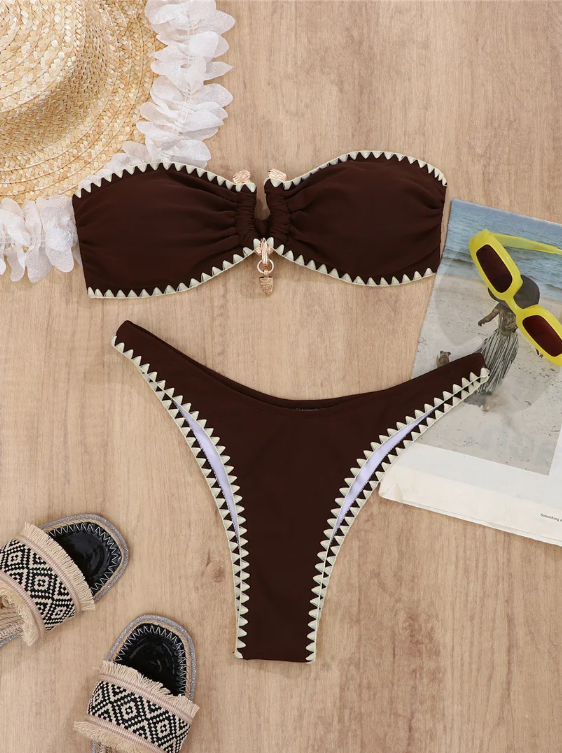 Chocolate brown bandeau bikini set with cream whipstitch trim, shell charm detail and high-leg bottoms in a flat lay.
