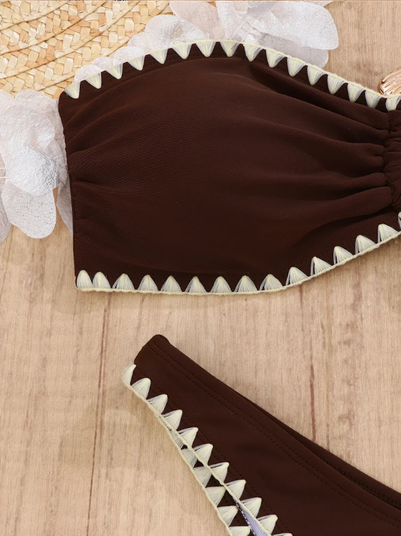 Close-up of chocolate brown swim fabric with cream whipstitch trim and gathered bandeau detailing.
