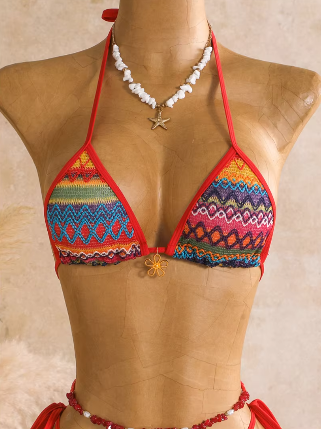 Close-up of rainbow textured triangle bikini top with multicolour zigzag pattern, red binding and gold-tone charm detail.
