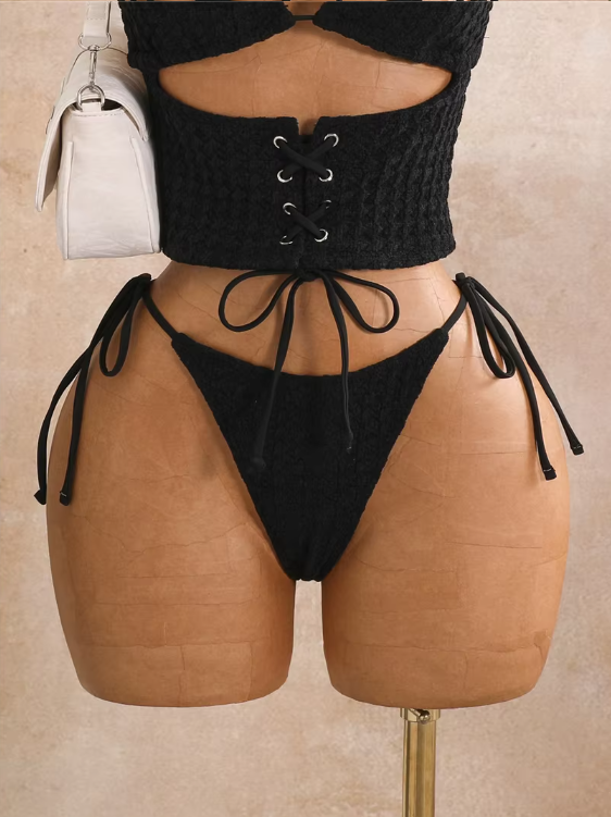 Close-up of black textured bikini set with lace-up waist panel, tie-side bottoms and high-leg silhouette.