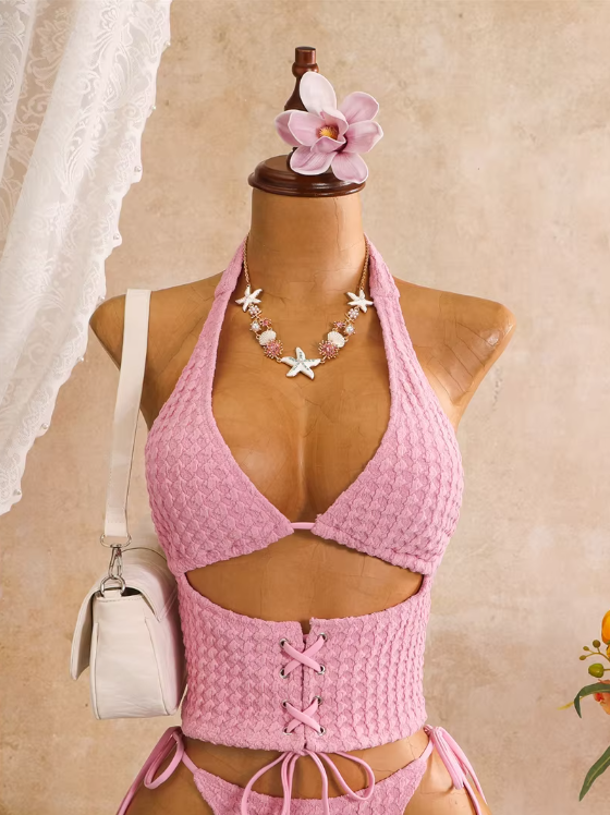 Close-up of pink textured halter bodice with sculpted front cut-out, shell necklace styling and lace-up waist panel.